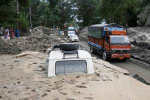 一輛停泊在路邊的吉普車被埋在近3英呎深的泥石流中。旁邊的通道則由救援隊伍連日清理打通。（圖：香港宣明會） <br/>