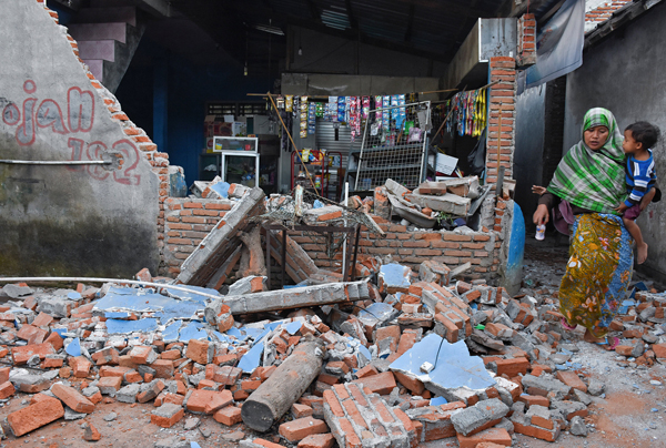 當地時間2018年8月5日，印度尼西亞龍目島地震致當地數千房屋被毀，圖為一名當地婦女抱著孩子經過房屋廢墟。 （圖：來自網絡）
