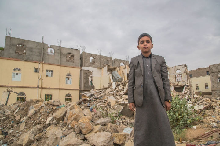 也門薩達一名兒童站在受破壞的建築物前。（圖：世界糧食計劃署） 