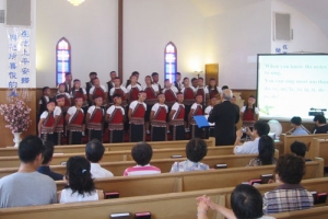 30位天真無邪的純樸原住民學童「台灣原住兒合唱團」穿著布農族服裝，以天籟之聲傳揚海外。昨日他們在信道會迦南堂縯齣，其中前立者為指揮寇順舉牧師。（圖：基督日報/全威） <br/>